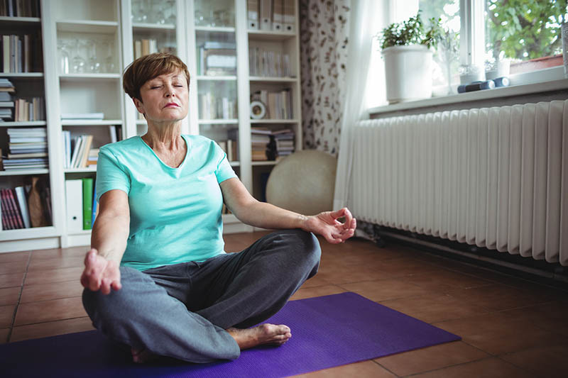 Senior woman meditating in lotus position at home