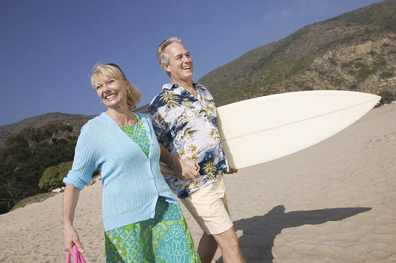 Senior Couple with surfboard smiling on beach